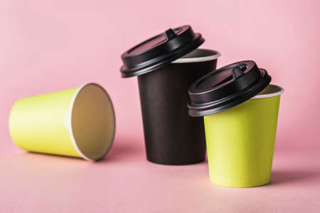 Some green and black paper reusable coffee cups with lids on a pink background. Zero waste concept close-up with copy space. Horizontal orientation.の写真素材