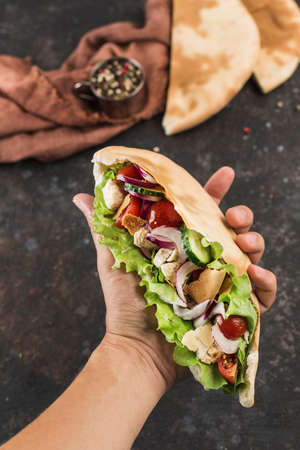 National Greek fast food pita with chicken and fresh vegetables in the male hand of the chef on a dark background, top view. Vertical orientation.の写真素材