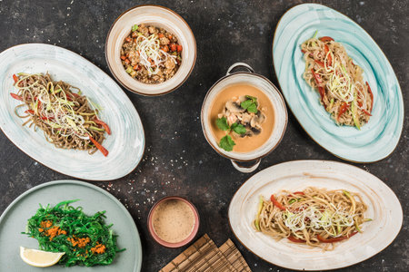 Several Asian dishes with noodles, rice and seaweed on different plates with the chef serving on a dark background. View from above with a copy-space. Restaurant food. Flat layの写真素材
