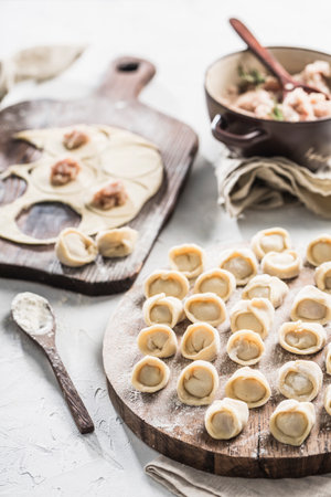 The process of cooking dumplings of Russian and Ukrainian national food. A lot of ready-to-cook pork dumplings on a large wooden board with flour on a light background. Side view. Vertical orientation. Close-up.の写真素材