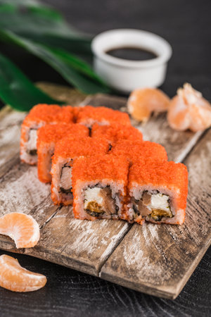 California roll with red caviar, salmon and tangerines in cream cheese on a dark background. Sushi menu. Japanese cuisine. Close-up, selective focus. Vertical orientation.の写真素材