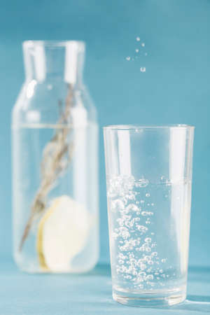 Glass and bottle with clear water, rosemary and lemon on a blue background close-up. The concept of drinking water for health. Vertical orientation with a copyspace. Selective focus.の写真素材