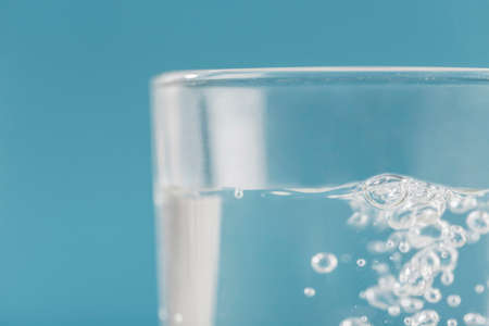 A glass of clear water and bubbles on a blue background close-up. The concept of drinking water for...