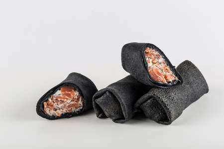 Black cuttlefish ink pancakes with salmon filling with cottage cheese on a white background close-up with copy space for text, isolated. Traditional food for the Maslenitsa holiday. Horizontal orientation.の写真素材