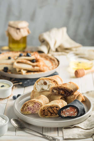 Several pancakes with different fillings on a plate on a wooden white background side view with a copy space for the text. Traditional food for the Maslenitsa holiday. Vertical orientation.の写真素材