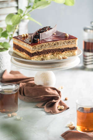 Chocolate cake with nuts on a wooden stand with a teapot and a cup of tea on a light background. Side view with a copy space for the text. Dessert for eating for the holidays. Vertical orientation.の写真素材