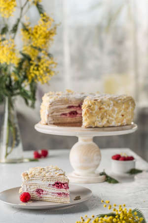 Napoleon puff cake with berry filling on a wooden stand with a cut piece on a plate. On the background of the home interior, a side view with a copy space for text. Russian birthday cake.の写真素材