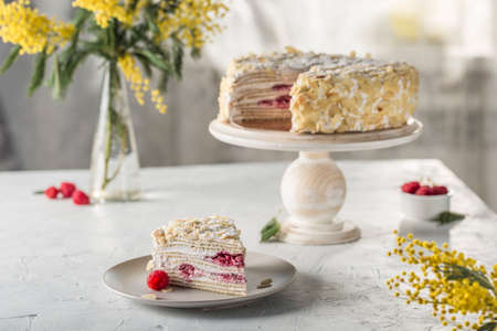 Napoleon puff cake with berry filling on a wooden stand with a cut piece on a plate. On the background of the home interior, a side view with a copy space for text. Russian birthday cake.の写真素材