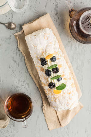 Meringue roll with berry filling on a napkin, with a teapot and a mug of tea on a light background. Top view with a copy space for the text. Dessert for the morning tea party.の写真素材