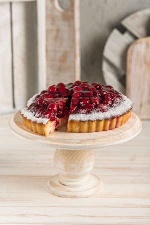 Cherry pie with a cut piece on a white wooden stand on a light background of the kitchen interior. Side view with a copy space for the text. Vertical orientation.の写真素材