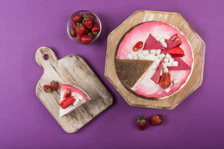 Biscuit cake with strawberry filling and fresh strawberries with a cut piece on a wooden stand on a...