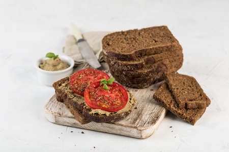 Black bread sandwich with tomatoes and hummus on a wooden board on a light background. Side view...