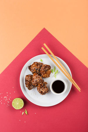 Fried chicken teriyaki with sesame seeds on a flat plate with lime, soy sauce and chopsticks on a bright colorful background. Asian food. Top view with a copy space for the text. Vertical orientation.の写真素材