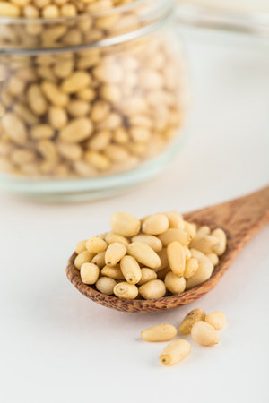 Peeled pine nuts on a wooden spoon and in a glass jar on a light background. A natural product for the diet. Side view with a copy space. Vertical orientation.の写真素材