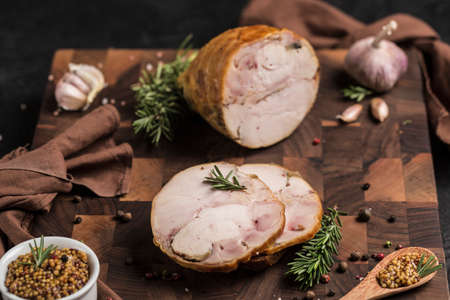 Chicken roulade is cut into two large pieces on a wooden board with fresh herbs and cherry tomatoes on a dark background. Side view. Horizontal orientation with a copy space for the text.の写真素材