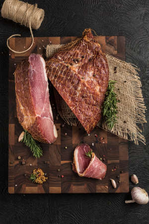 Smoked prosciutto on a wooden board with grainy mustard and fresh herbs on a dark background. Top view. Vertical orientation with a copy space for the text.の写真素材