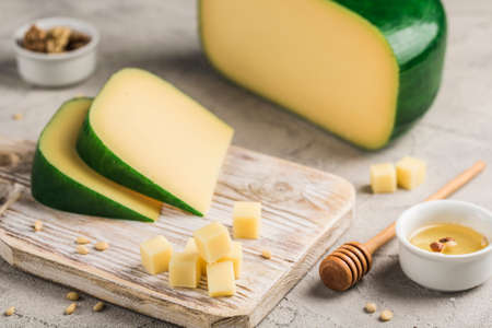 Traditional hard Parmesan cheese is cut into pieces on a light wooden board with honey and nuts. An excellent product for cooking poultry dishes, soups, pasta. Light wooden background. Side view.の写真素材