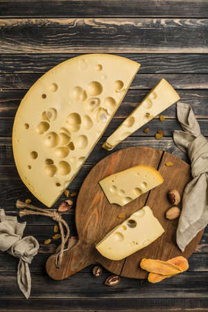 Maasdam cheese of natural aging is enriched with beneficial bacteria. The cheese is cut into pieces on a dark wooden board. Dark wooden background. Top view with a copy space for the text.の写真素材