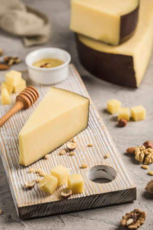 Traditional hard Parmesan cheese is cut into pieces on a light wooden board. An excellent product for cooking poultry dishes, soups, pasta. Light wooden background. Side view.の写真素材