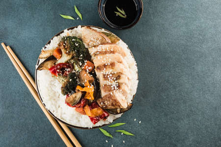 Bowl with rice, grilled vegetables and teriyaki chicken with chopsticks and soy sauce on a dark background. Asian food. horizontal orientation. Top view with a copy space for the text.の写真素材