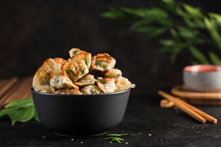 Fried dumplings with pork and herbs in a black round bowl on a dark background with chopsticks. Korean food. Side view with copy-paste for text. horizontal orientation.の写真素材