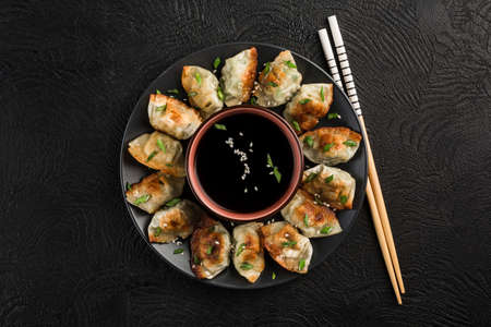 Fried dumplings with pork and herbs on a black round plate with soy sauce in the center on a dark background with chopsticks. Korean food. Top view with a copy-paste for the text.の写真素材
