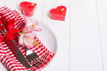 Valentine's day table setting. Fork, knife with red ribbon and little flowers on the plate with red...