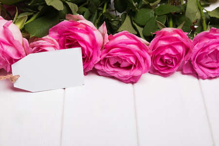 Beautiful pink roses and empty paper card on the white wooden table, close-upの写真素材