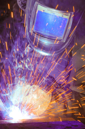 Welder on the production of weld metal. Sparks fly smoke