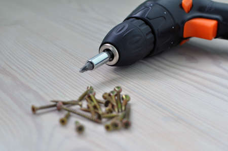 Electric screwdriver and screws on a wooden table.