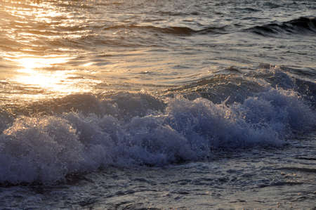 Tropical sunset background. Beautiful colorful ocean wave breaking closing near sand beach. Glare on...
