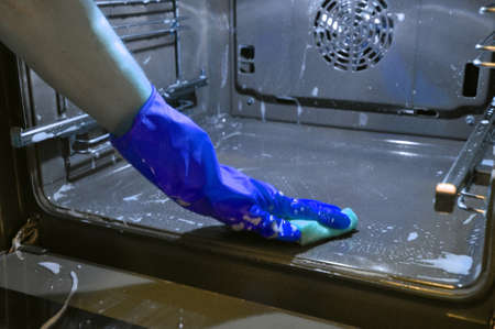 cleaning the oven in the kitchen. hand in a blue household glove.