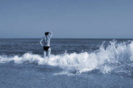Young beautiful woman. A woman in a black swimsuit enjoys walking on the sea waves and takes sunbathing on the beach. tinting, blueprintの写真素材