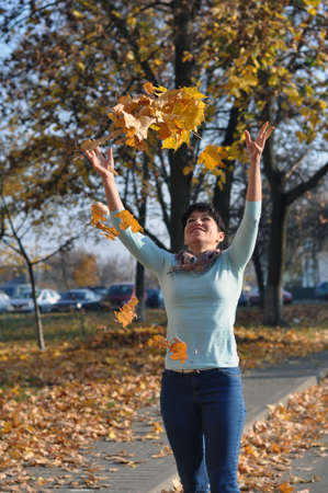season and people concept - happy young woman throwing maple leaves and having fun in autumn parkの写真素材