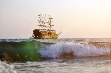 Tropical sunset background. Beautiful colorful ocean wave. Pleasure ship with masts on the horizon. Recreationの写真素材