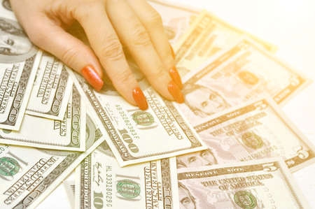 Female fingers with long artificial manicured nails hold a wad of money. U.S. dollars