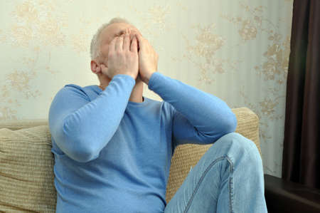 Young man in a blue sweater with a headache at home sitting