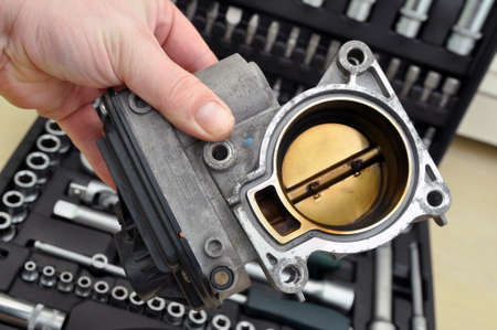 Repair and cleaning the car throttle. Throttle with traces of burning and soot on the background of a set of tools for car repairの写真素材