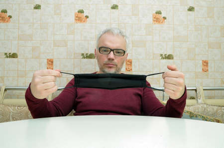 COVID-19. Stay home and distance yourself. A young man in a black medical mask is sitting at home....