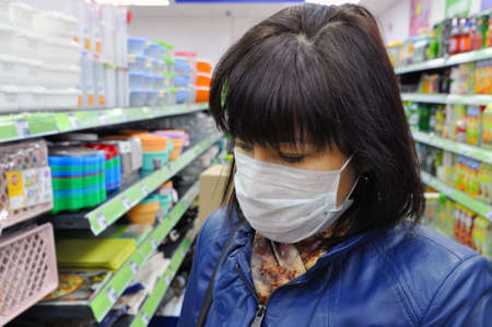 Young European woman in a blue leather jacket and a mask against infections in the store. Protecting...