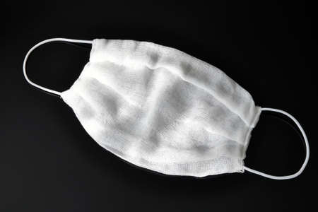 Gauze bandages with elastic bands over the ears, made at home, on a black background. Respiratory...