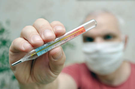 A mercury thermometer indicating a high temperature is in the hands of a sick man. The man is out of focus.の写真素材