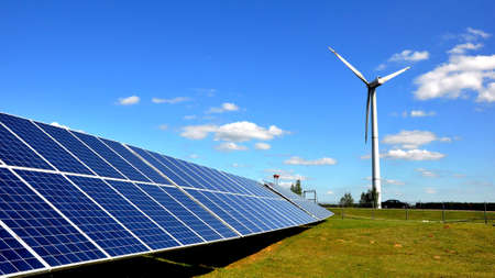 Solar panels and a wind turbine against a deep blue sky with clouds. Green energy