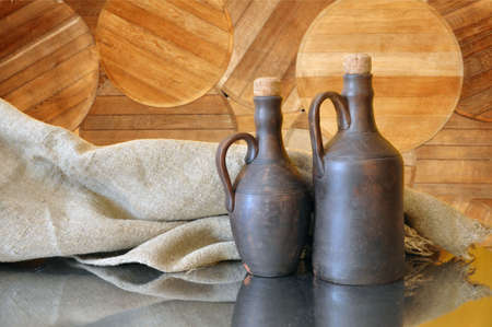 Old clay bottles for storing oil, wine on the background of round oak dons from barrelsの写真素材