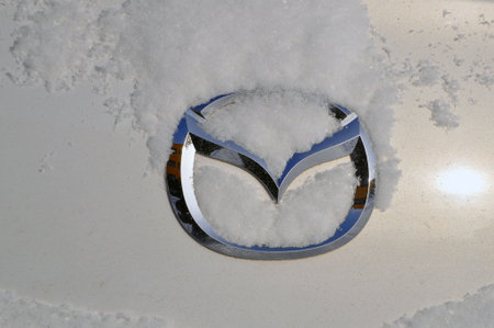 Mazda car logo on the trunk lid under a layer of snow. Winter.のeditorial素材