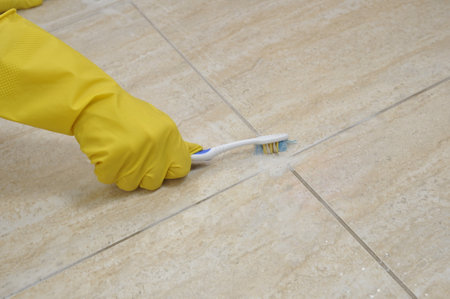Cleaning tile joints with a toothbrush. Yellow rubber household gloves.の写真素材