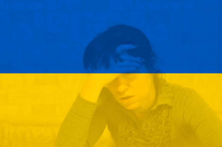 A woman with a headache holds her head against the background of the flag of Ukraine. military conflict.の写真素材