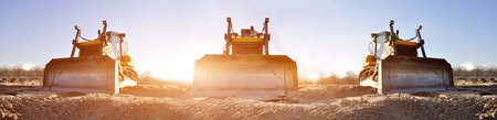 Crawler bulldozers on a construction site against the backdrop of the rising sun.