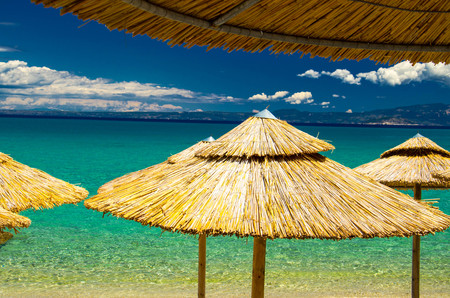 View of blue azure paradise water of Toroneos kolpos gulf, blue sky, white clouds over Sithonia peninsula, yellow straw beach umbrellas parasol in Pefkohori, Halkidiki, Kassandra, Macedonia, Greeceの写真素材
