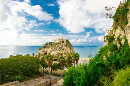 Monastery Sanctuary church of Santa Maria dell Isola on top of rock of Tyrrhenian Sea and green palm trees, blue sky with white clouds around, Tropea town, Vibo Valentia, Calabria, Southern Italyのeditorial素材
